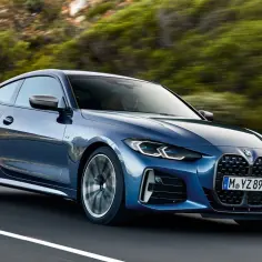 Niebieskie BMW Gran Coupé pędzi po krętej drodze wśród zielonych wzgórz.