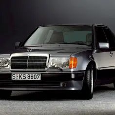 Klasyczny w124 Mercedes, szary sedan z charakterystyczną kratką i felgami, prezentuje się elegancko na ciemnym tle.