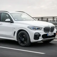 Białe BMW X5 M50d pędzi po autostradzie, błyszcząc w pochmurny dzień.