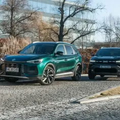 Zielony MG ZS Classic i czarny SUV na tle nowoczesnego budynku. Klasyka i nowoczesność w jednym kadrze.