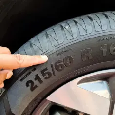 Palec wskazujący na oznaczenia na oponie samochodowej, w tym rozmiar 215/60 R16.