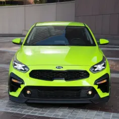 Jaskrawozielony Kia Forte z czarnym grillem i detalami, zaparkowany na brukowanym placu przed budynkiem.