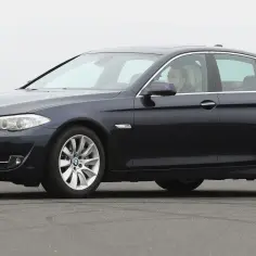 Ciemnogranatowe nowe BMW 5 na drodze, z kierowcą za kierownicą. Eleganckie linie i sportowy wygląd.