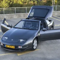 Szary Nissan 300zx z otwartymi drzwiami i bagażnikiem, gotowy do jazdy.