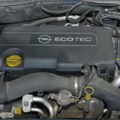 Silnik Ecotec z Opla Astry H. Widoczny jest czarny plastikowy dekiel z logo Opla i napisem Ecotec, a także elementy układu dolotowego i akumulator Varta.