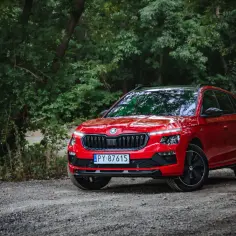 Czerwona Skoda Kamiq Monte Carlo zaparkowana na leśnej drodze, otoczona bujną zielenią.