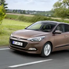 Brązowy Hyundai i20 jedzie po wiejskiej drodze. Wiele osób chwali ten model, a jego opinie są pozytywne.