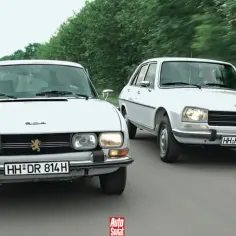 Dwa białe Peugeot 504 jadące obok siebie po wiejskiej drodze.
