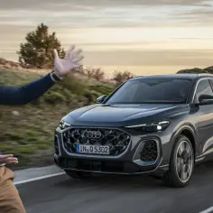 Mężczyzna prezentuje Audi Q5, podkreślając jego imponujące audi q5 wymiary. Jazda po malowniczej drodze o zachodzie słońca.