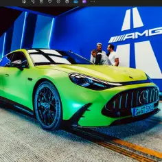 Jaskrawozielony Mercedes GT 63 z czarnymi felgami prezentuje się imponująco na tle niebieskiej ściany z logo AMG.