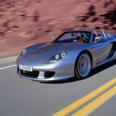 Srebrny Porsche Carrera GT pędzi po pustynnej drodze, tworząc wrażenie prędkości.