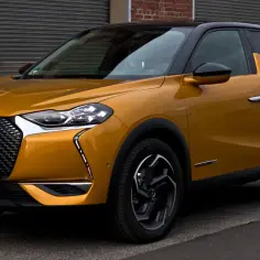 Złoty DS3 Crossback z czarnym dachem, zaparkowany przy ceglanej ścianie.