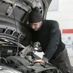 Mechanik z latarką bada silnik Renault, szukając przyczyny błędu DTC P0380.