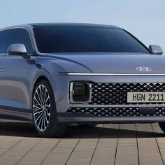 Elegancki, szary Hyundai Grandeur z charakterystycznym pasem świateł LED i siatkową atrapą chłodnicy, zaparkowany nad brzegiem morza.