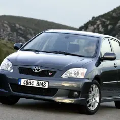 Ciemnoszara Toyota Corolla E12 z hiszpańskimi tablicami rejestracyjnymi jedzie po krętej drodze wśród wzgórz.