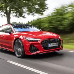 Czerwone Audi RS7 Sportback pędzi po drodze, otoczone zielenią drzew.