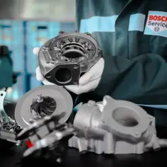 Mechanik w białych rękawiczkach prezentuje turbosprężarkę, kluczowy element silników tdi. W tle logo Bosch Service.