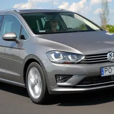 Szary Volkswagen Sportsvan jedzie po drodze, kierowca w okularach prowadzi auto.