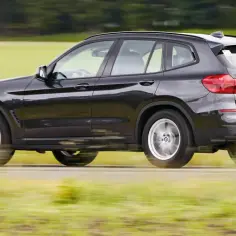Czarne BMW X3 w ruchu, z rozmazanym tłem pól i drzew. Wiele osób szukało BMW X3 opinie, a ten SUV świetnie się prezentuje.
