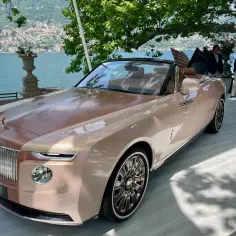 Elegancki Rolls-Royce Boat Tail w kolorze szampańskim, prezentowany nad jeziorem Como, z otwartymi drzwiami i luksusowym wnętrzem.