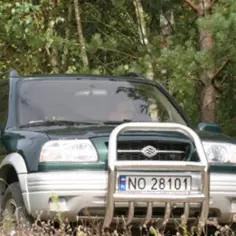 Zielony Suzuki Grand Vitara 2 z osłoną zderzaka i polską tablicą rejestracyjną NO 28101 na tle lasu.