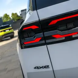 Nowy Jeep Compass 4xe z charakterystycznymi czerwonymi światłami z tyłu, zaparkowany obok nowoczesnego budynku.