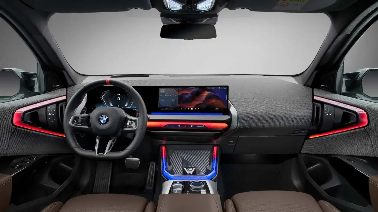 Nowoczesne wnętrze BMW X3 z dużym ekranem i ambientowym oświetleniem. Kierownica i deska rozdzielcza sugerują pozytywne bmw x3 opinie.