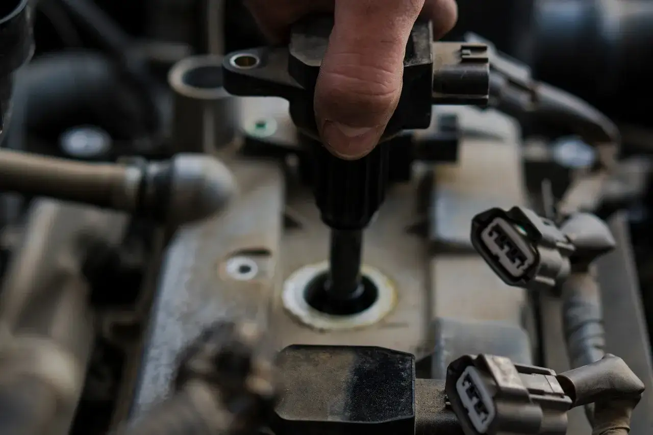 Dłoń mechanika wymienia cewkę zapłonową. Objawy awarii mogą być różne, od nierównej pracy silnika po problemy z odpalaniem.