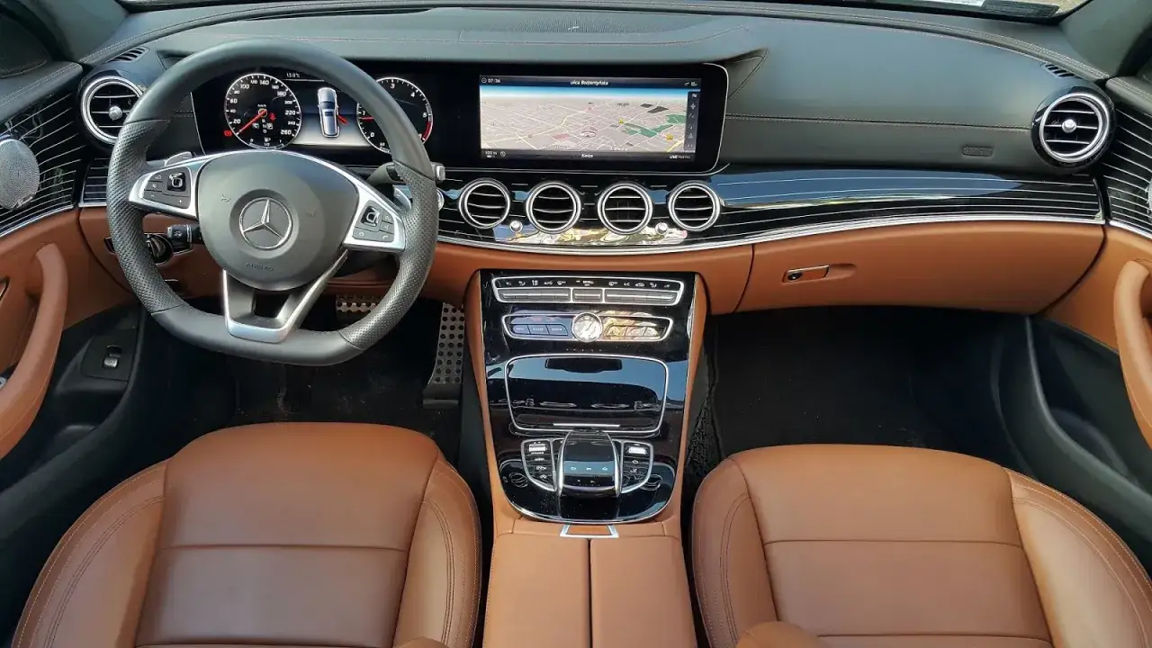 Wnętrze mercedesa e220d z brązową skórzaną tapicerką, nowoczesnym panelem i ekranem nawigacji.
