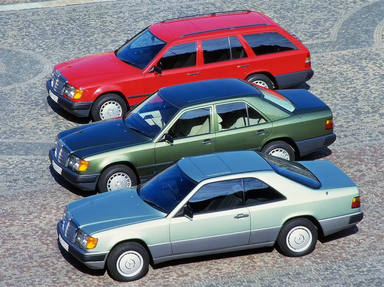 Trzy klasyczne modele w124: czerwone kombi, zielony sedan i błękitne coupe, stoją obok siebie na brukowanej nawierzchni.