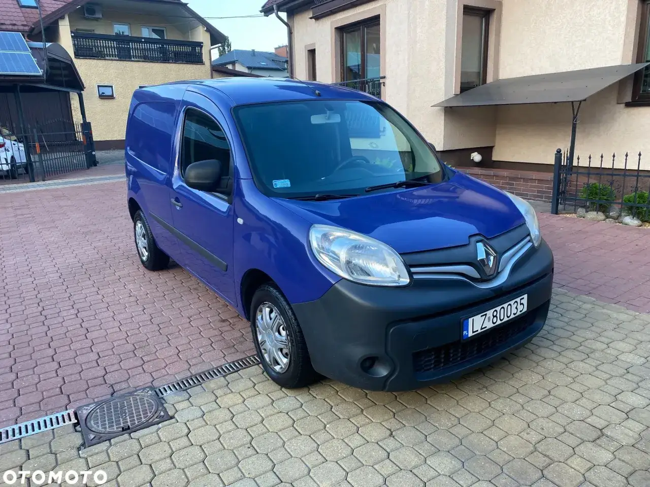 Niebieski Renault Kangoo 1.5 dCi zaparkowany na podjeździe z kostki brukowej przed domem.