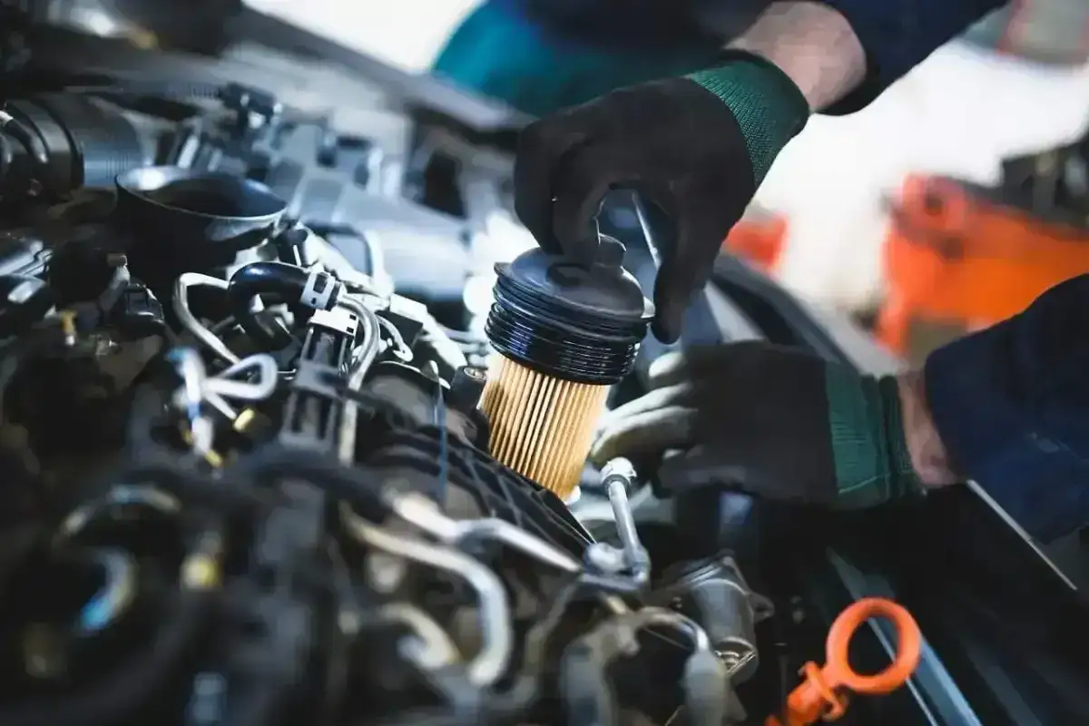 Mechanik w czarnej rękawiczce wymienia żółty filtr paliwa w silniku samochodu.