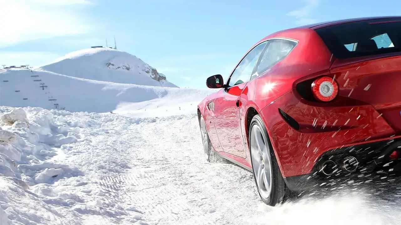 Czerwone Ferrari FF pokonuje ośnieżone górskie drogi, zostawiając za sobą ślady na śniegu.