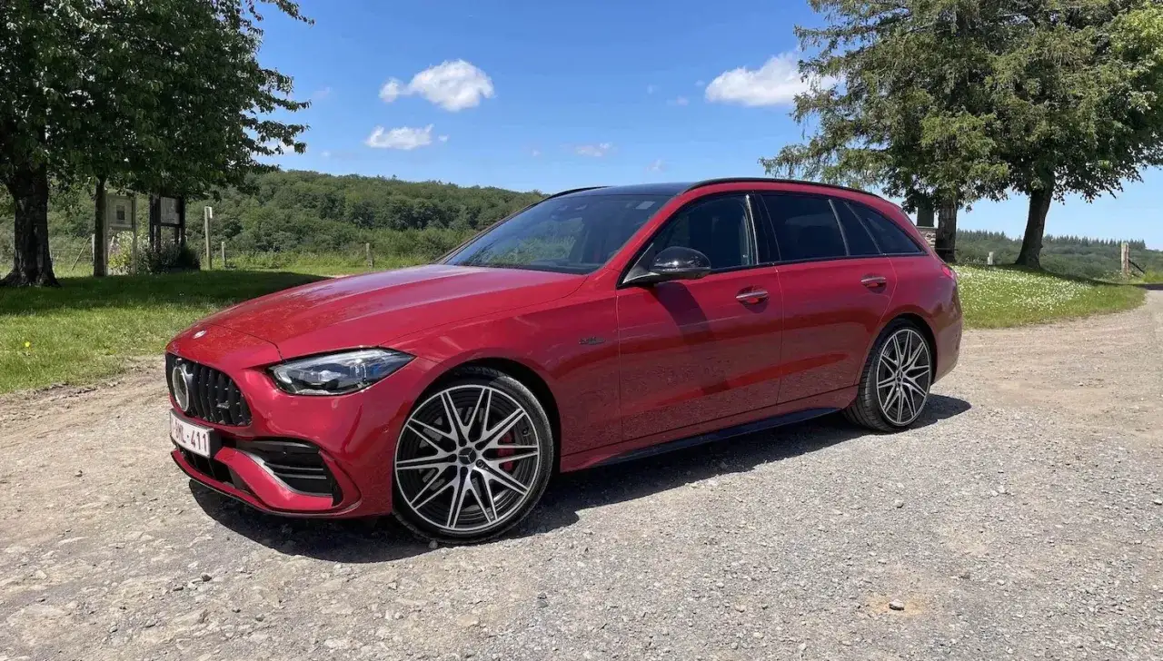 Czerwony Mercedes C43 AMG kombi zaparkowany na szutrowej drodze, otoczony zielenią i błękitnym niebem.