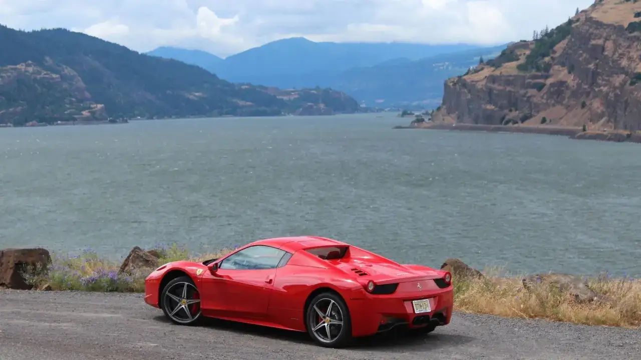 Czerwone Ferrari Italia zaparkowane nad jeziorem, w tle góry i skaliste klify.