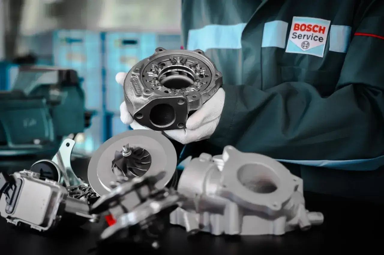 Mechanik w białych rękawiczkach prezentuje turbosprężarkę do silnika tdi. W tle logo Bosch Service.