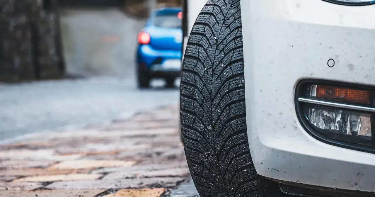 Białe auto z oponami zimowymi latem, gotowe na nieoczekiwane zmiany pogody. W tle niebieski samochód.