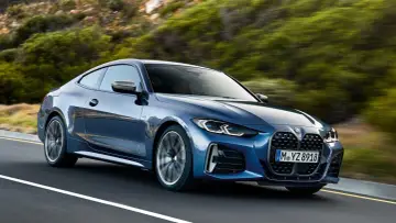 Niebieskie BMW Gran Coupé pędzi po krętej drodze wśród zielonych wzgórz.