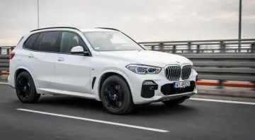 Białe BMW X5 M50d pędzi po autostradzie, błyszcząc w pochmurny dzień.