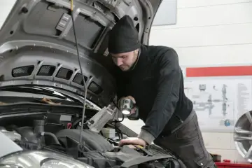 Mechanik z latarką bada silnik Renault, szukając przyczyny błędu DTC P0380.