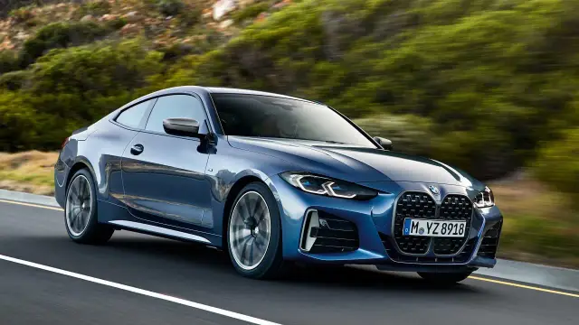 Niebieskie BMW Gran Coupé pędzi po krętej drodze wśród zielonych wzgórz.